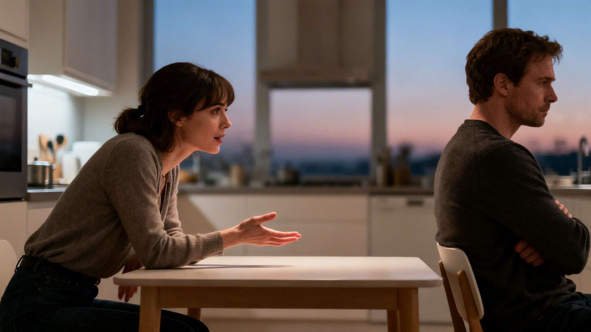A distressed woman gestures at a man turned away, showing relationship tension in a modern kitchen.