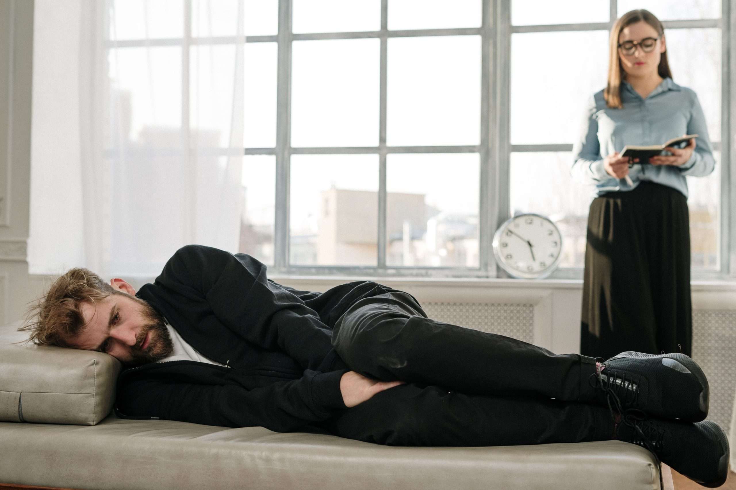couples therapy exercises for emotional intimacy - Psychological therapy session with a male patient lying on a couch and a female therapist taking notes.