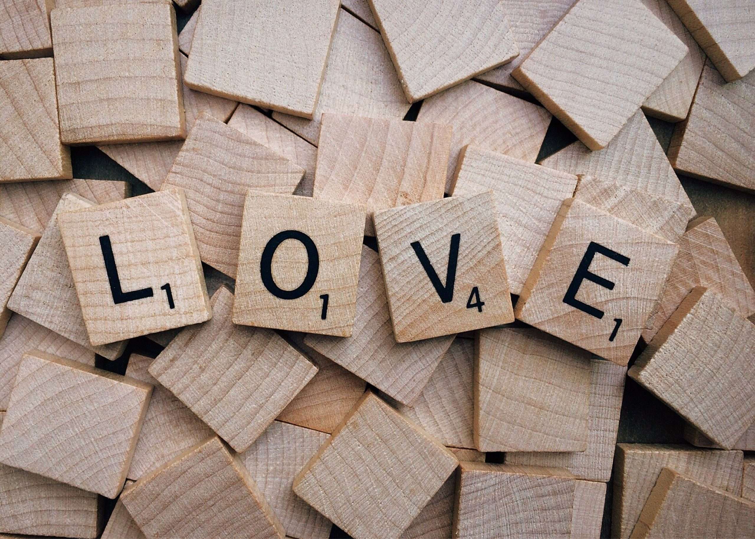 examples of love language - Scrabble tiles arranged to spell 'love' on a wooden background, conveying affection.