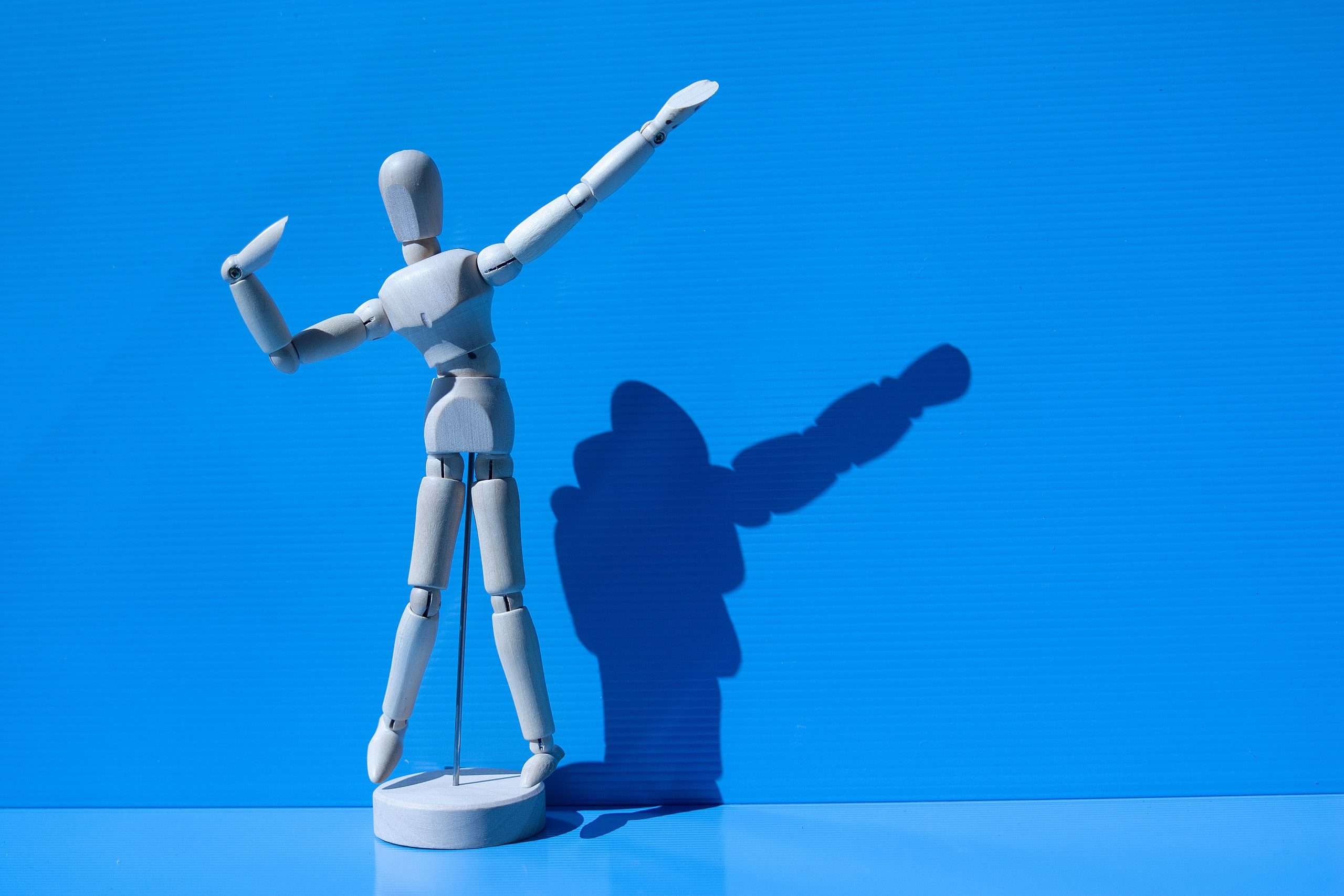 examples of love language - Wooden mannequin striking a pose with a dramatic shadow against a vibrant blue background.