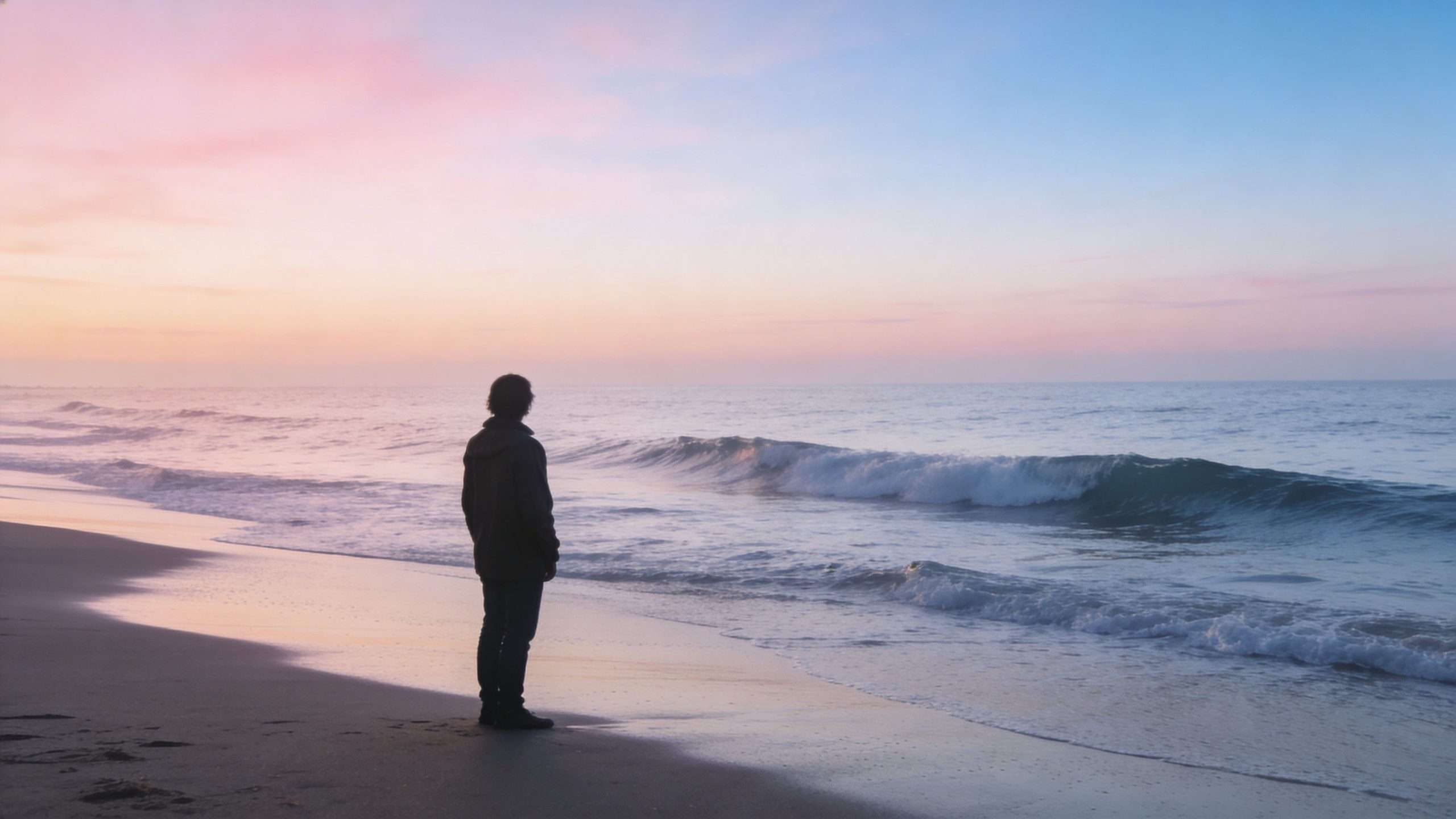 A silhouette of a person standing alone on a peaceful beach during a soft sunset.
