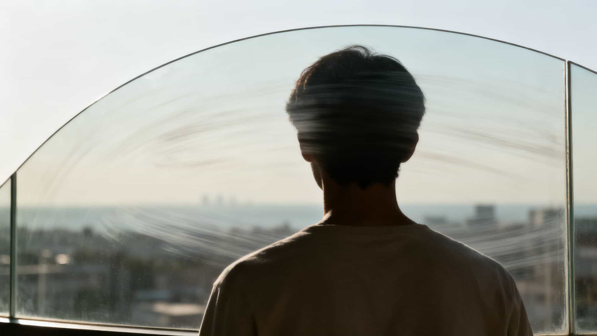 A person from behind looks out a dirty window at a blurry cityscape and horizon.
